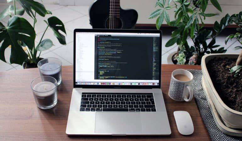 macbook pro beside white ceramic mug on brown wooden table